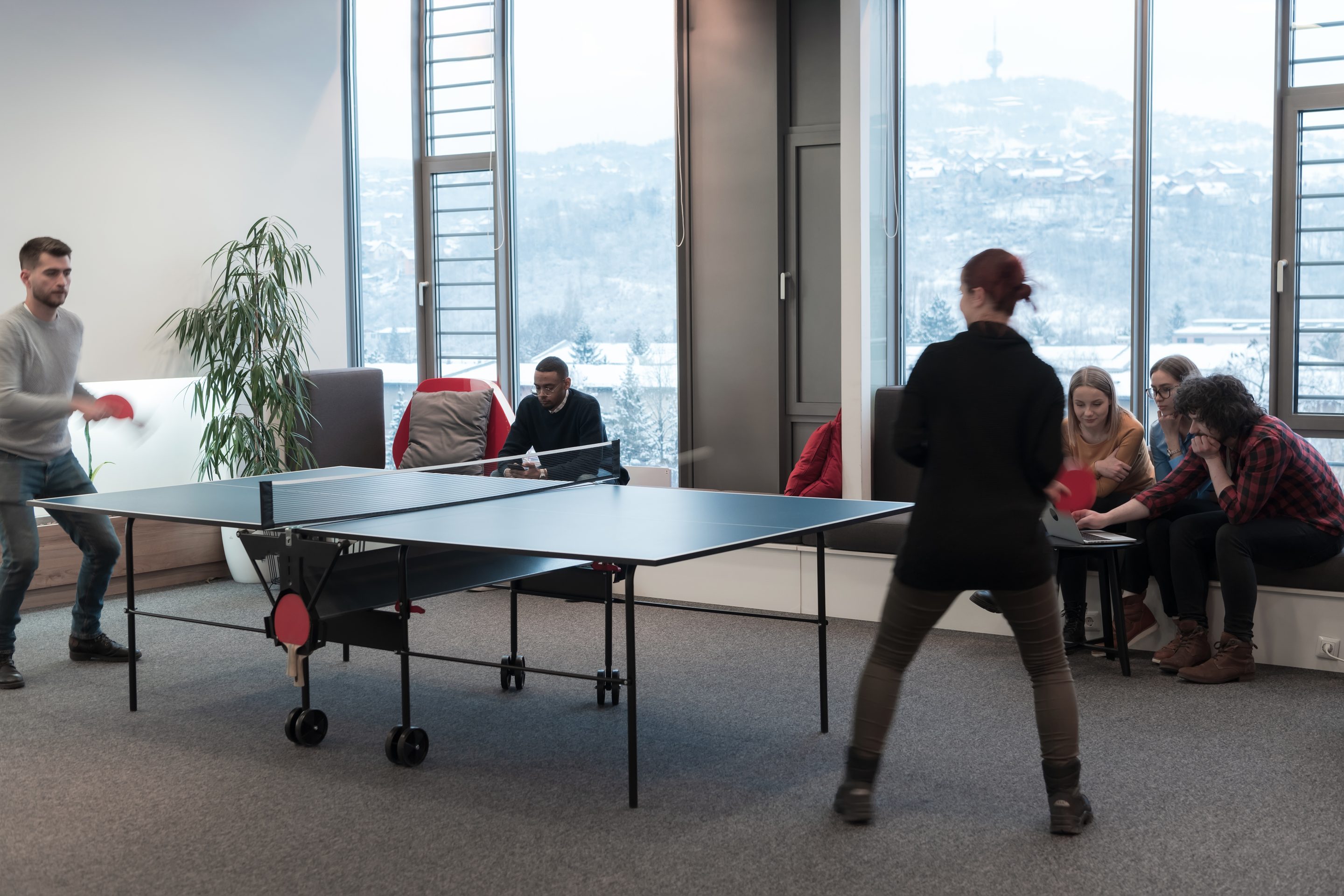 Jeunes hommes et femmes d'affaires en démarrage jouant au tennis de table dans un espace de bureau moderne et créatif. Des groupes de personnes se réunissent et font du brainstorming en arrière-plan